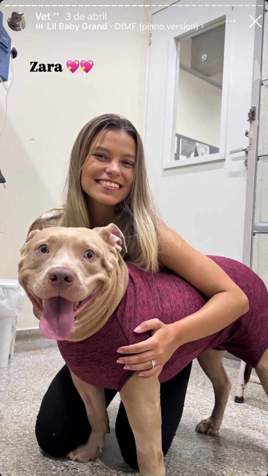 Alicia abraçando a cachorra Zara, vestida com roupa cirúrgica, na clínica